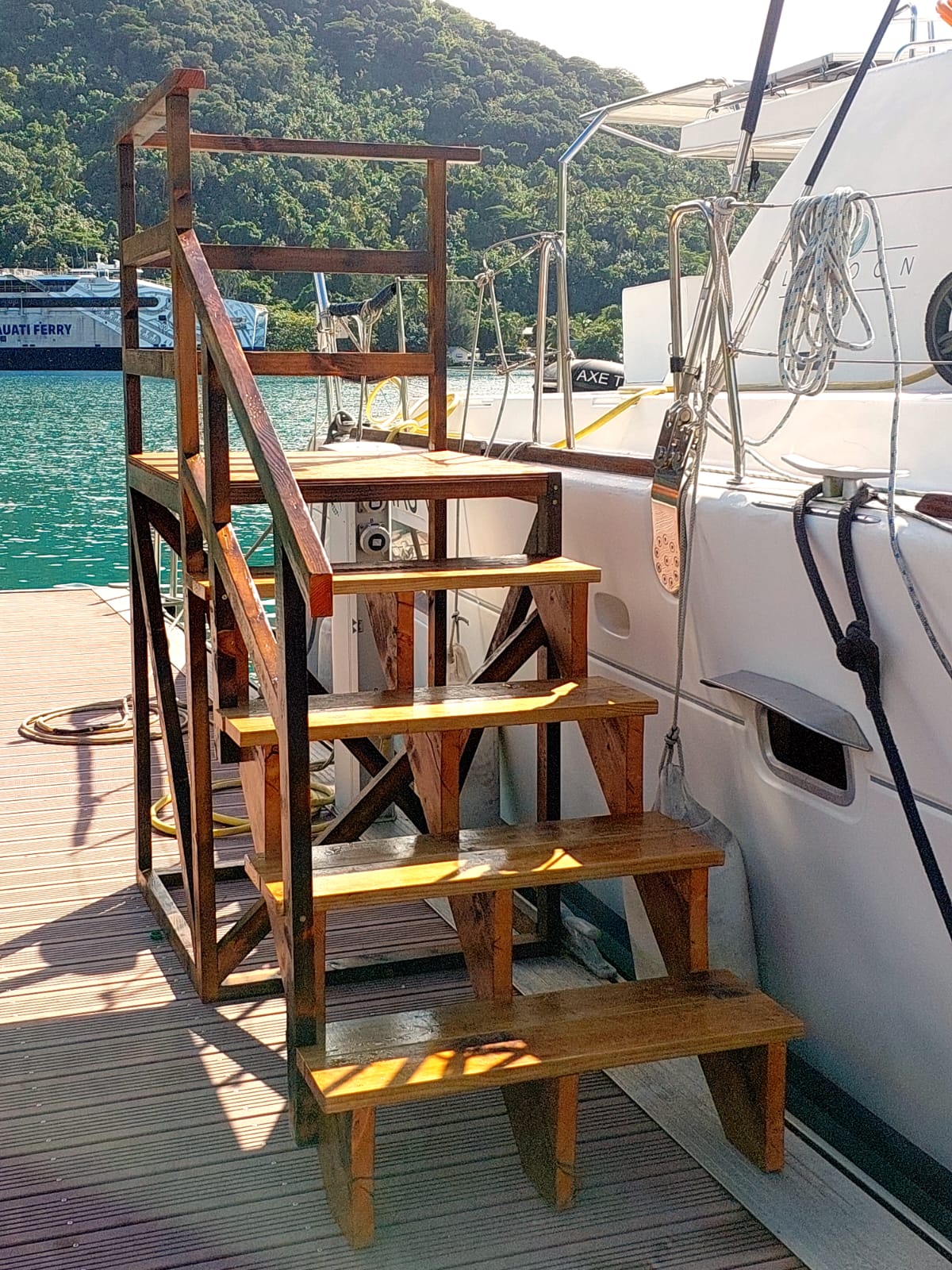Wooden boarding steps with a handrail leading from the marina dock to TUATAU V