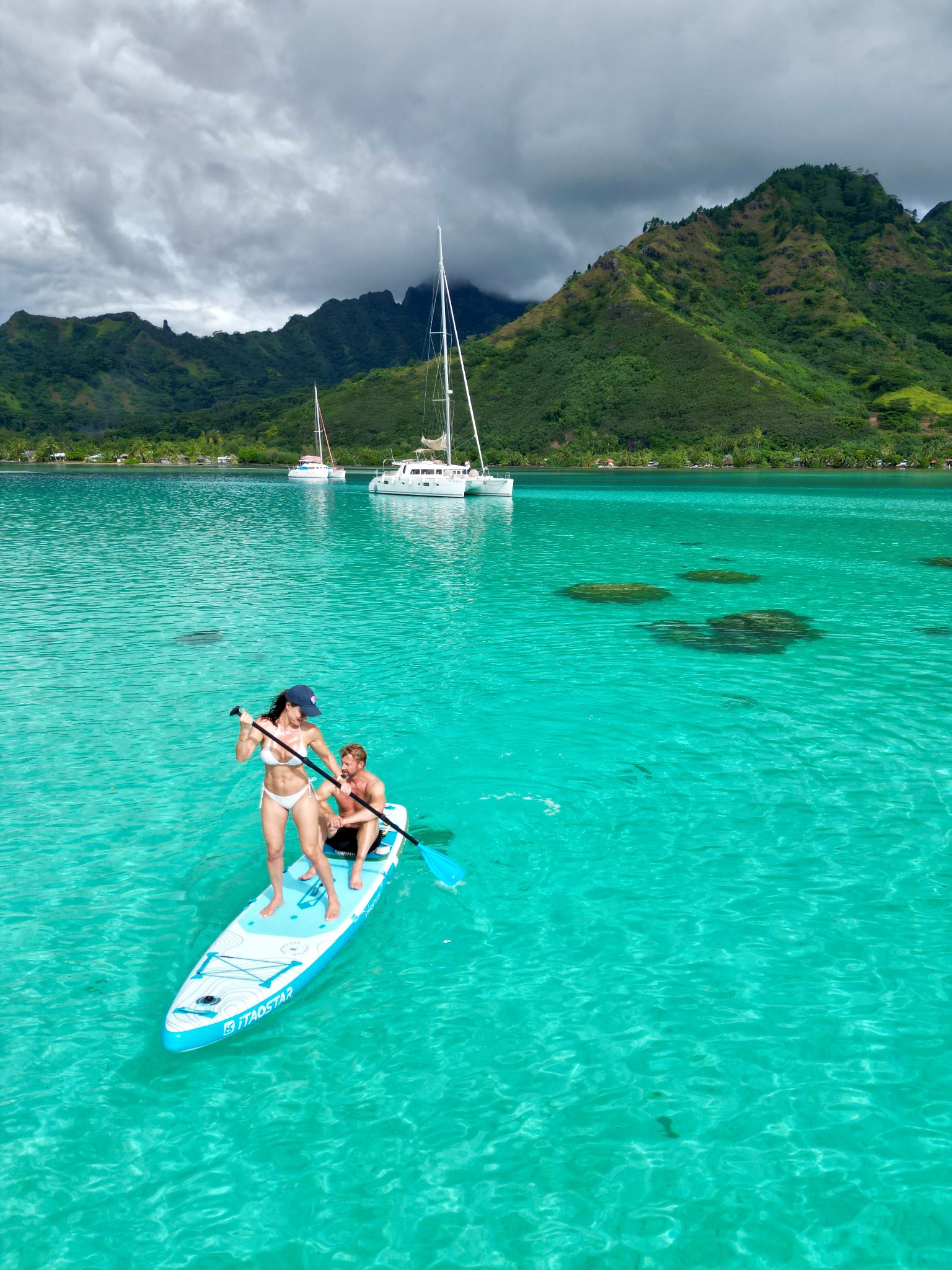 Paddleboarding in clear lagoon water with catamarans and Moorea’s mountains behind