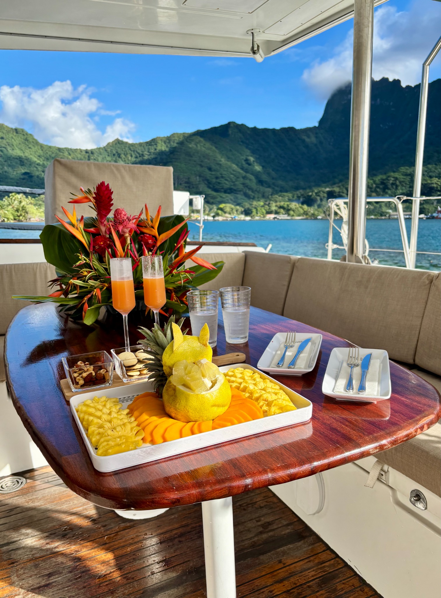 Welcome punch drinks and fresh tropical fruits on the catamaran table with Moorea’s mountains beyond